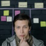 Thoughtful man pondering ideas in creative workspace with sticky notes behind.